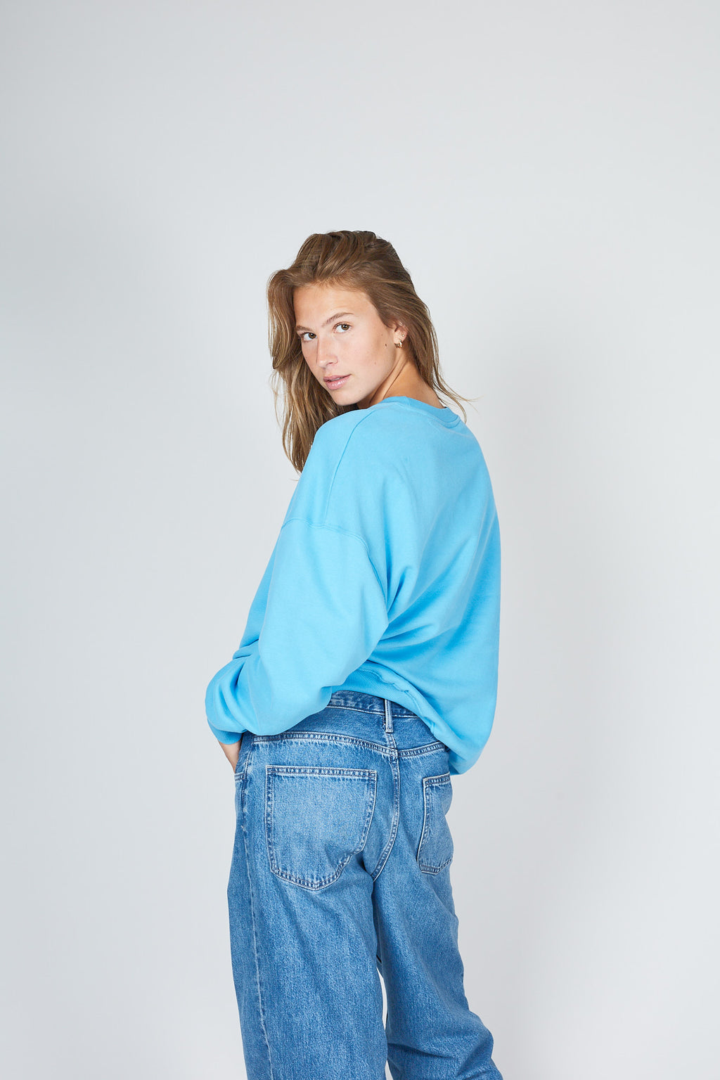 Person wearing a light blue oversized sweater and jeans on a white background